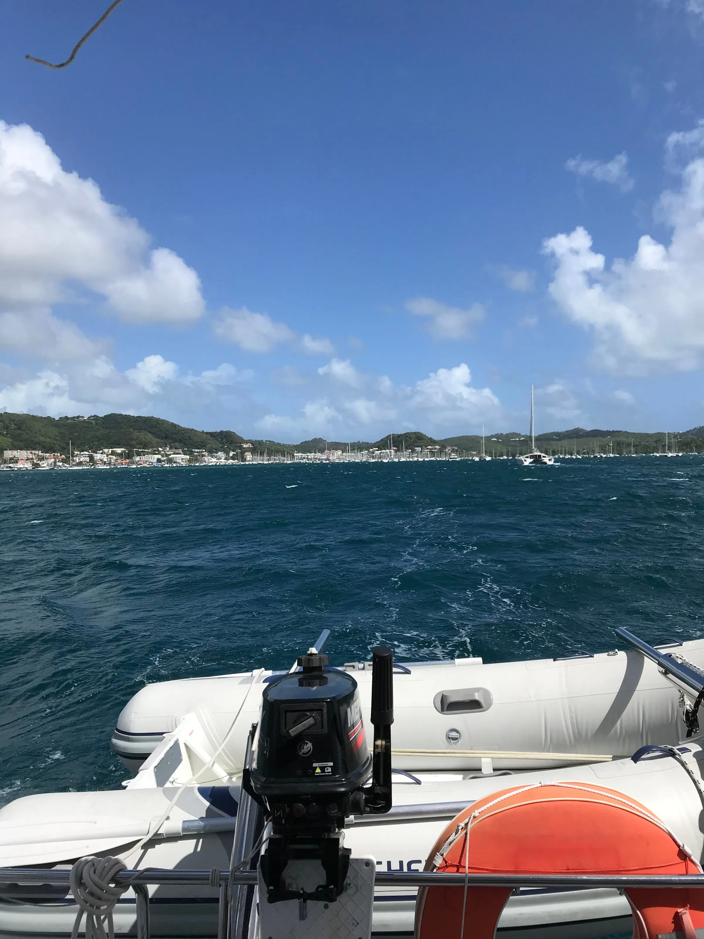 The tender and its outboard motor at the stern of the catamaran, with Le Marin marina and its yachts in the distance.