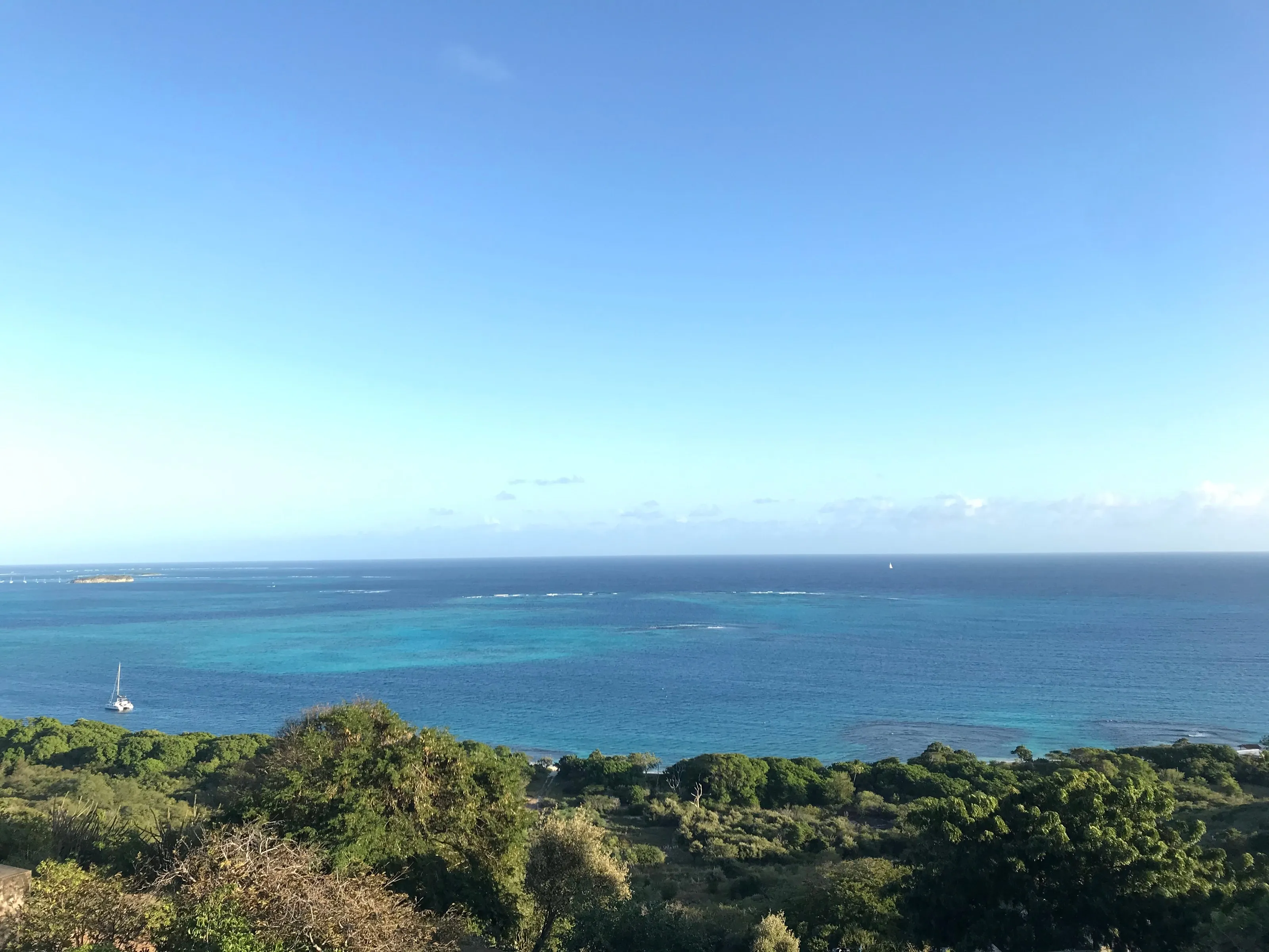 A turquoise lagoon and its reefs seen from a hill on Mayreau, with one catamaran at anchor.