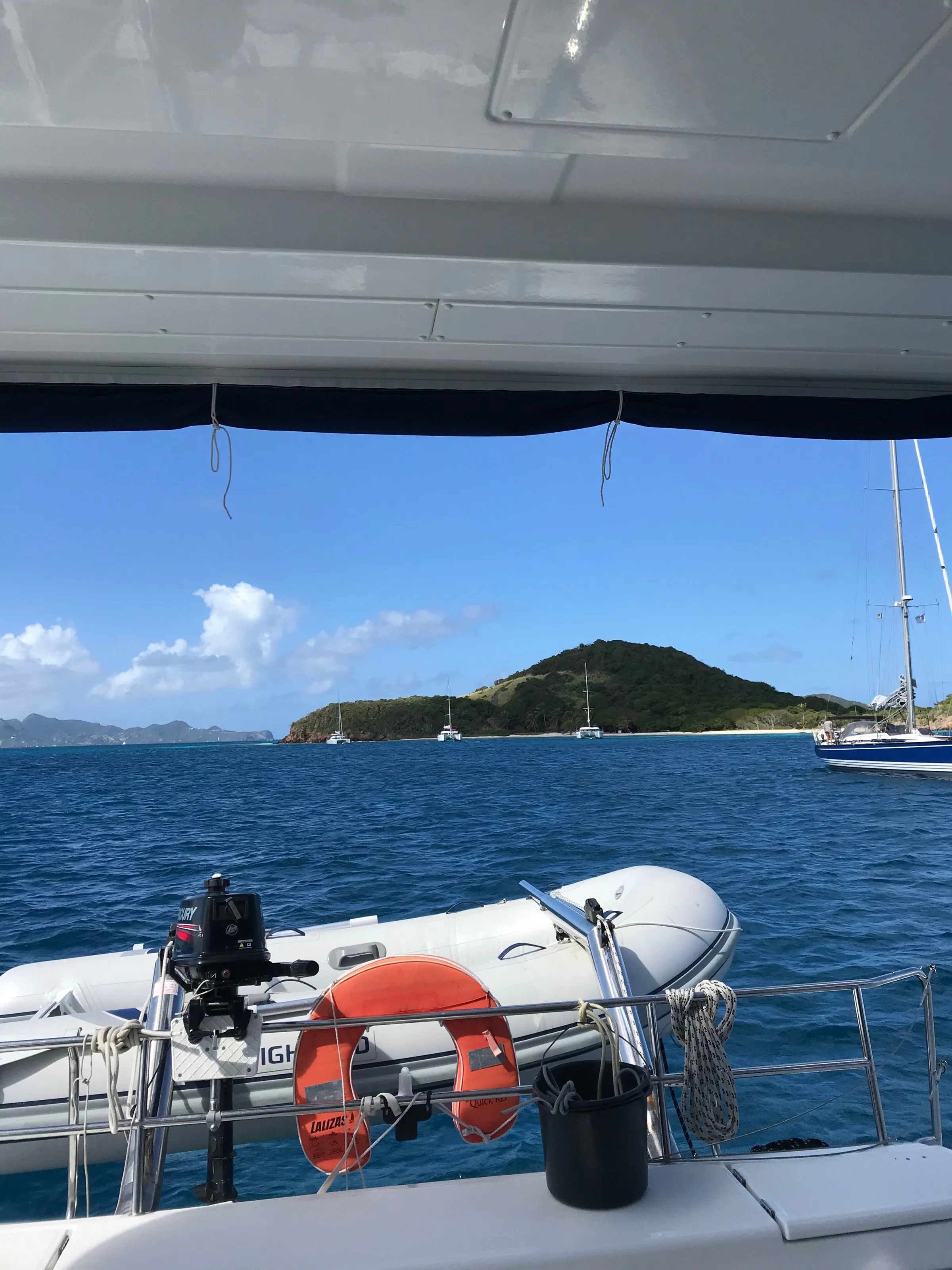 The tender at the catamaran's stern, with a small green island and several yachts at anchor beyond.