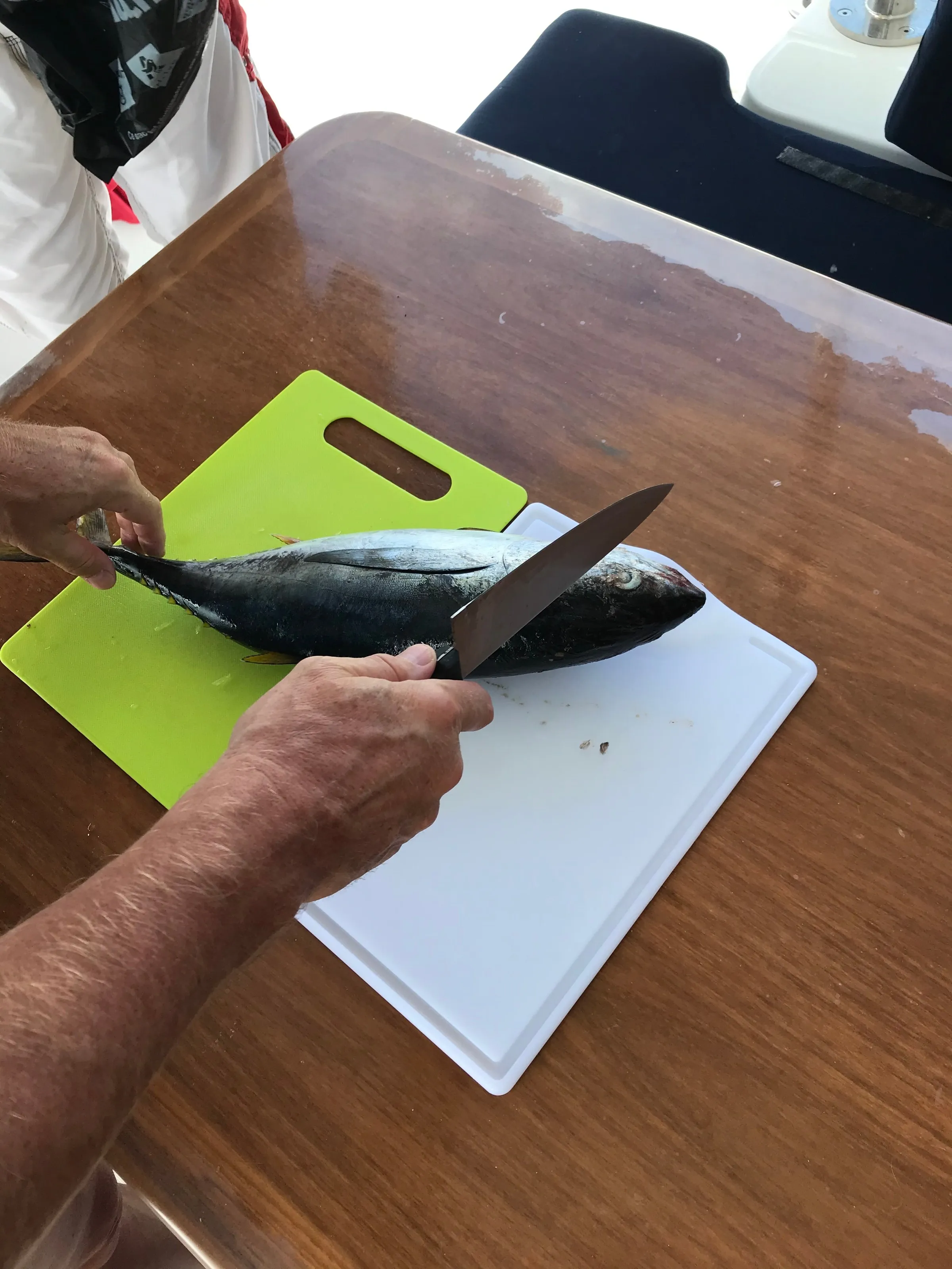 Hands cutting up a fish across two boards on the cockpit's wooden table.