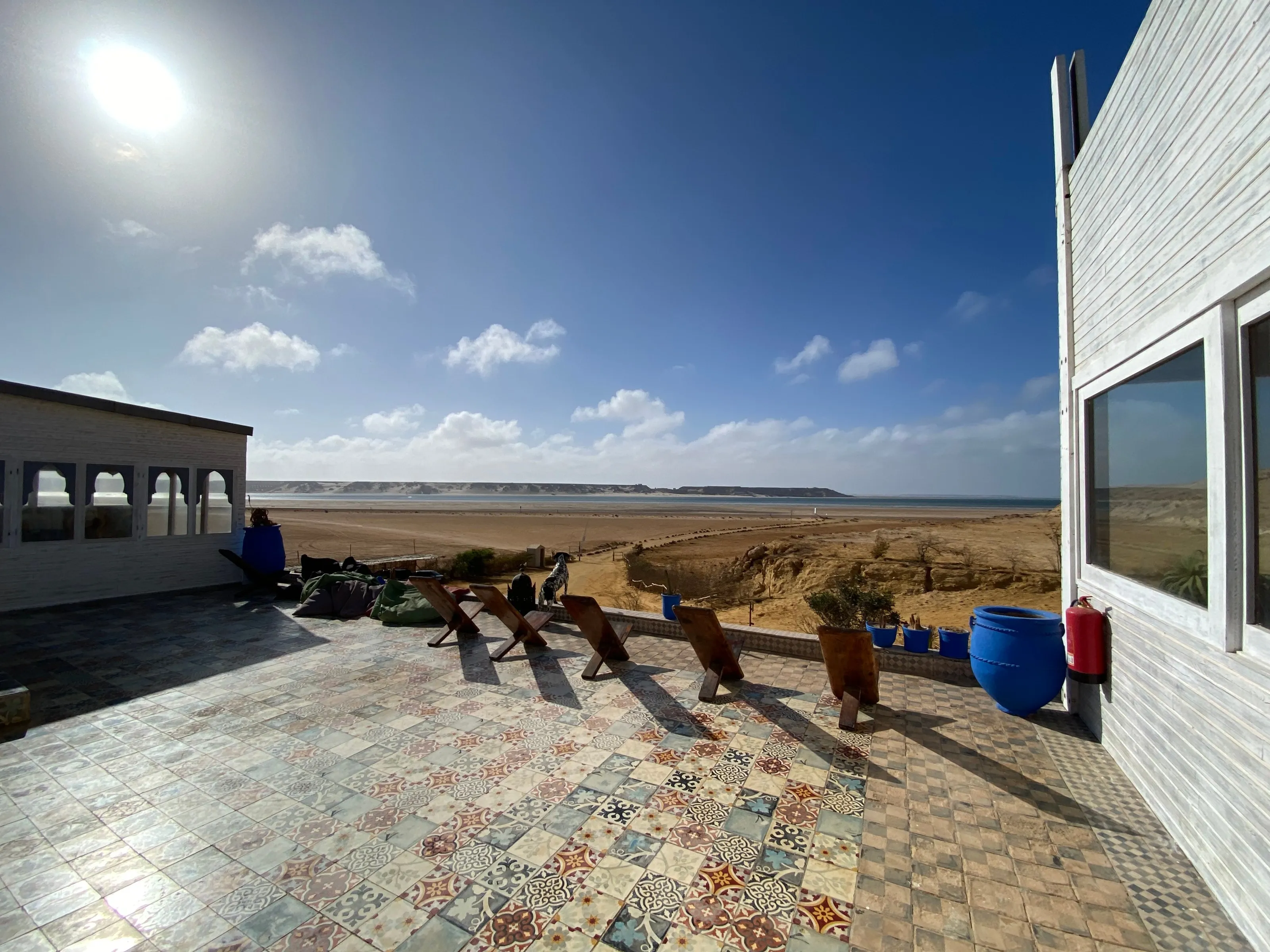 The camp's tiled terrace facing the sand and lagoon, with wooden chairs and large blue pots.