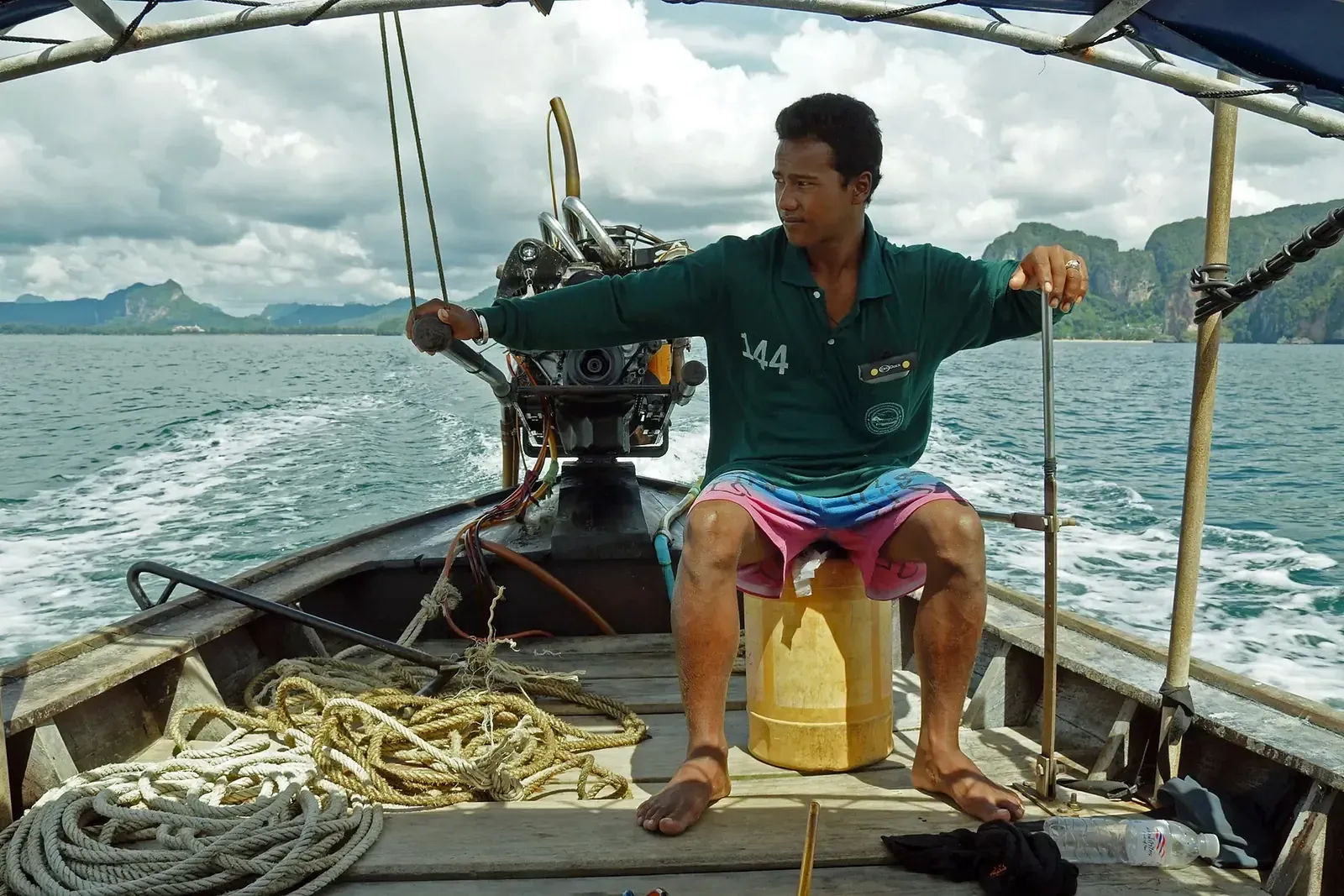 A long-tail boat captain at the helm, limestone islands behind him.