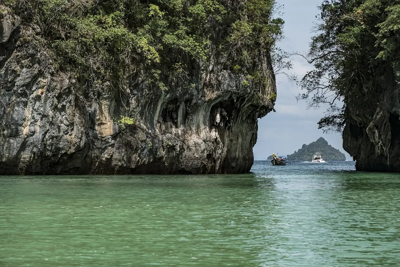The entrance to a lagoon between limestone cliffs, with boats in the distance.