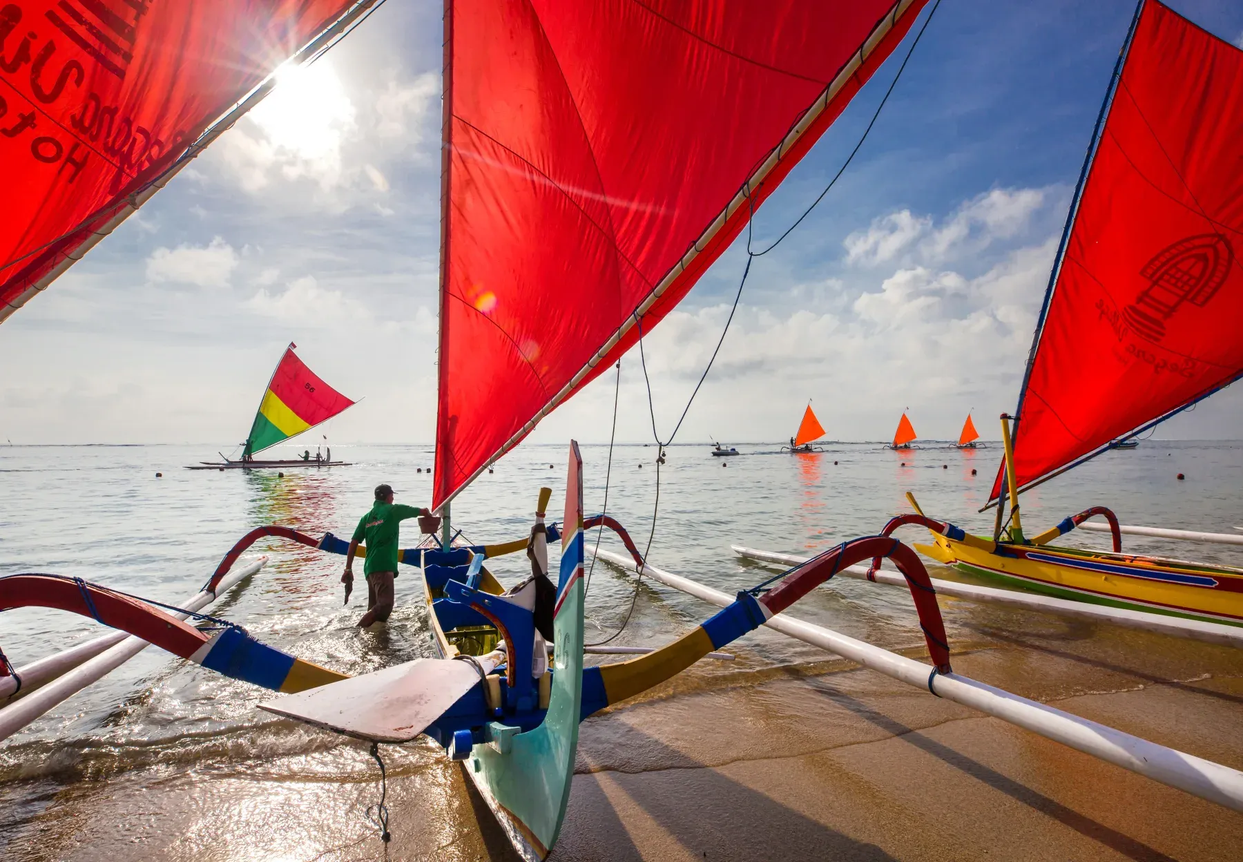 A fisherman seen from behind among jukung boats on Sanur Beach.