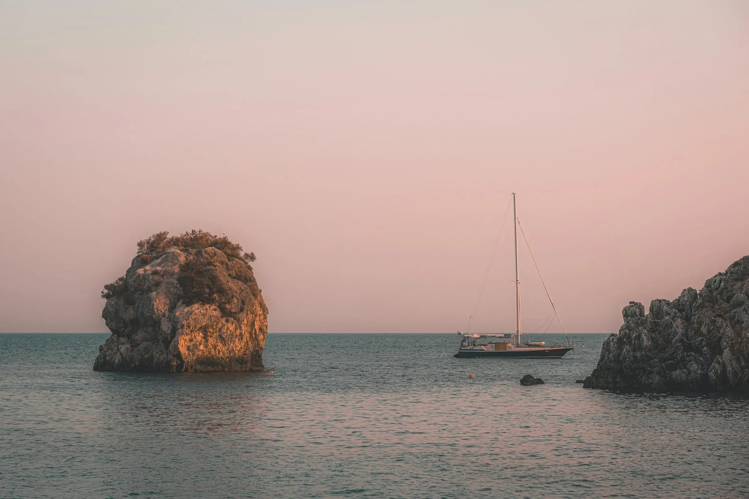 A lone sailboat at anchor at dusk, between two rocks, in Parga